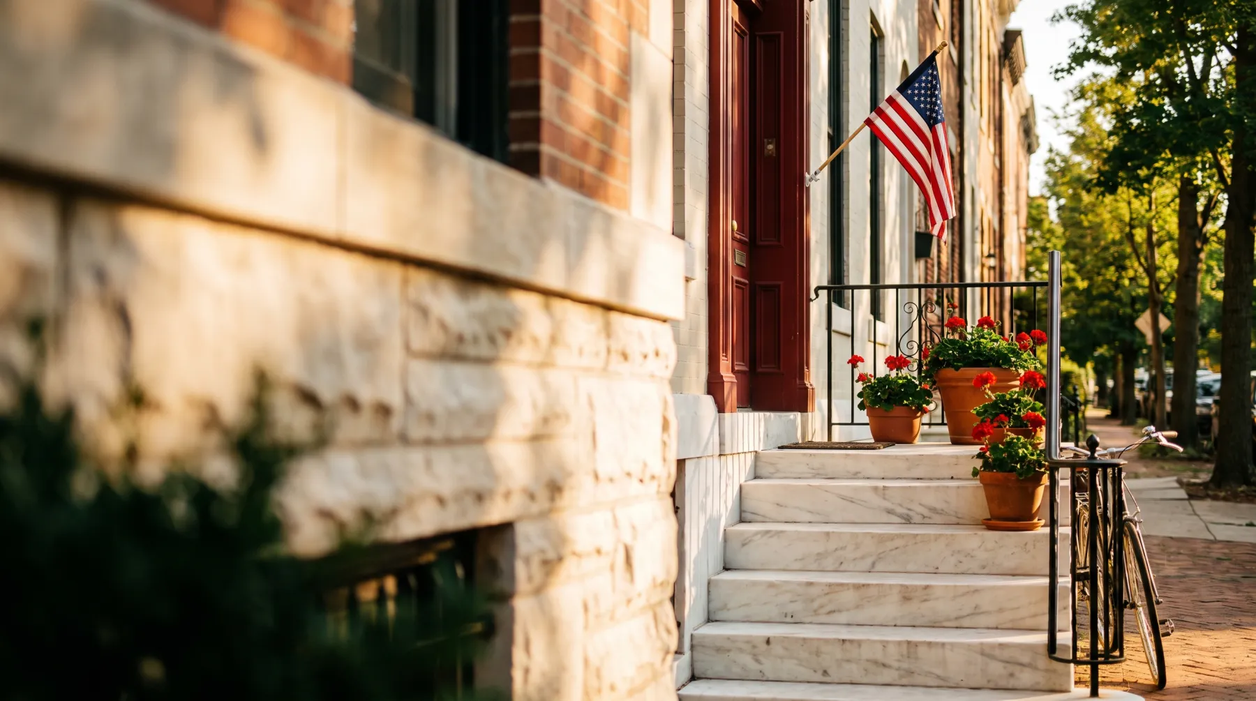 Marble rowhouse stoop with red door, flag, and geraniums — Baltimore